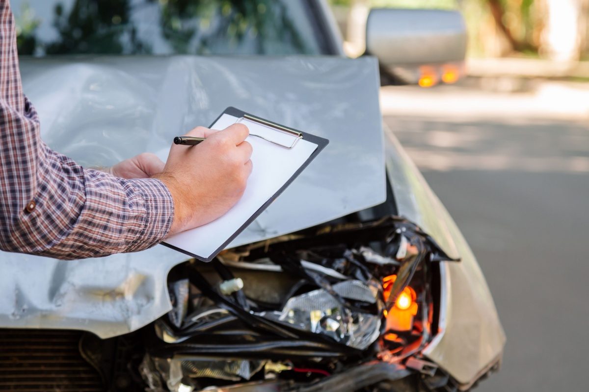 An assessor writing on a clipboard beside a damaged car