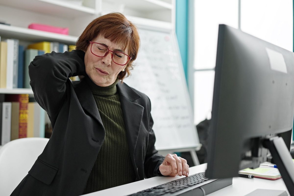 A school staff member at a desk holding the back of their neck