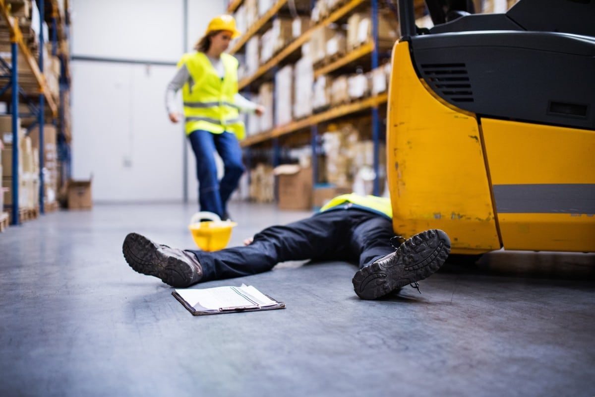 A worker on the floor of a warehouse beside a forklift
