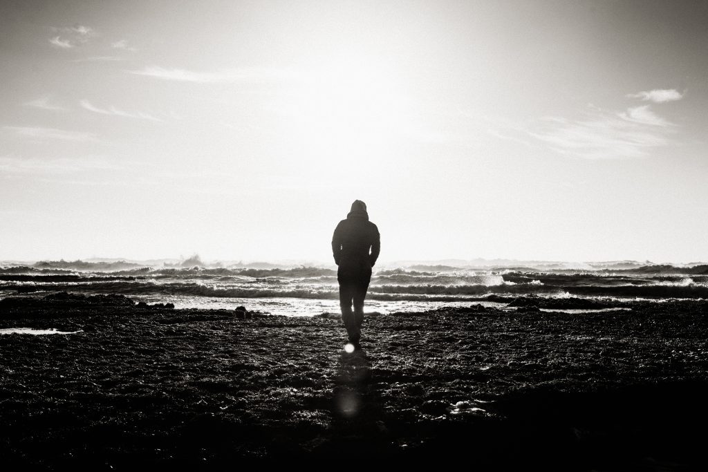 A distant lone figure walking on a shore, in black and white