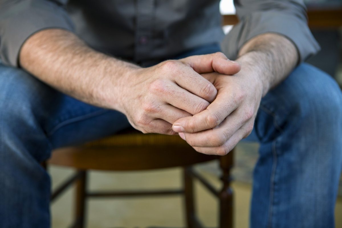 A person sitting with their hands clasped, seen from the chest down